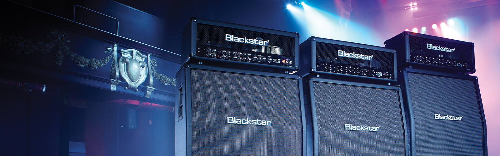 three stacks of Blackstar Series One guitar amp heads and cabs on stage with mult-colored lights behind them