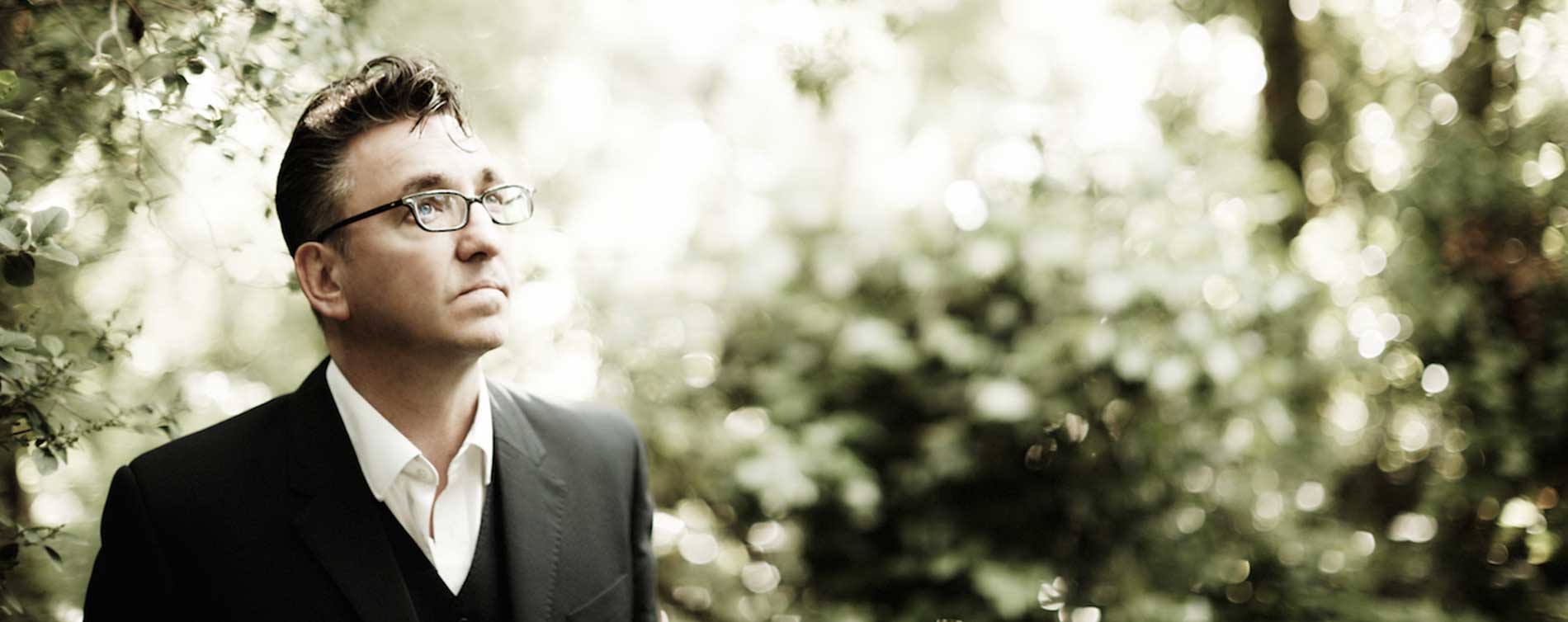 Richard Hawley wearing a black suit and eyeglasses